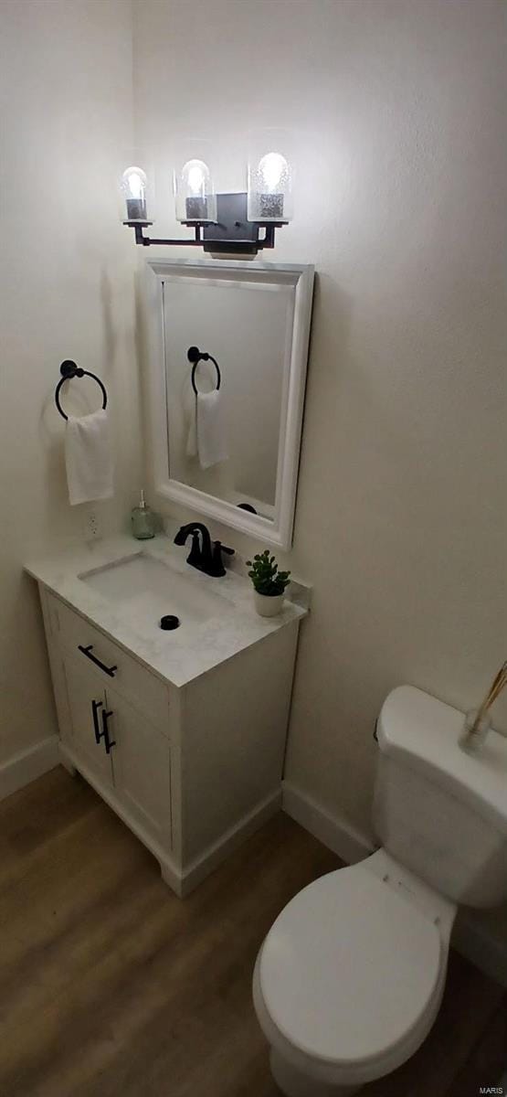 half bath featuring wood finished floors, vanity, toilet, and baseboards
