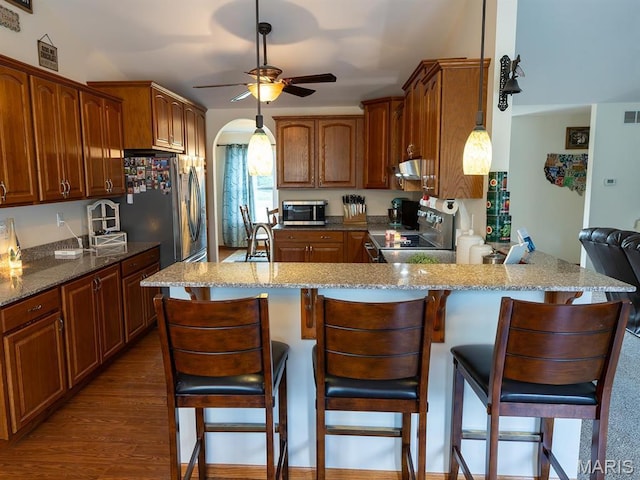 kitchen with stainless steel appliances, ceiling fan, under cabinet range hood, a peninsula, and light stone counters