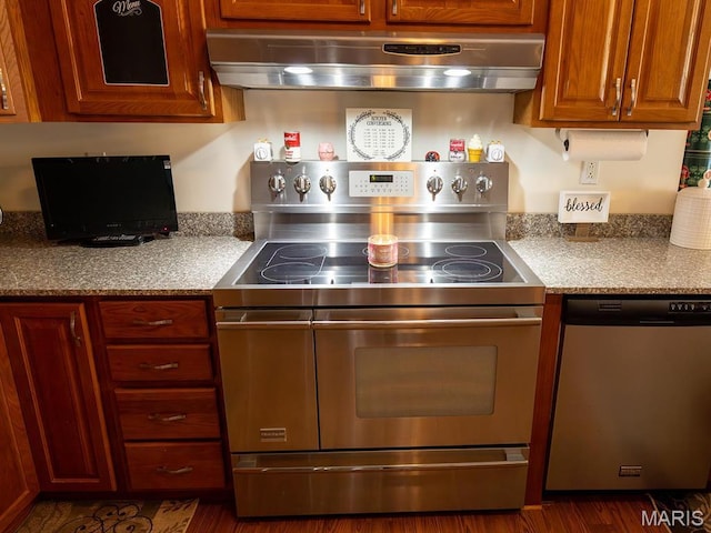 kitchen with stainless steel appliances, wall chimney range hood, dark wood-style flooring, and light countertops