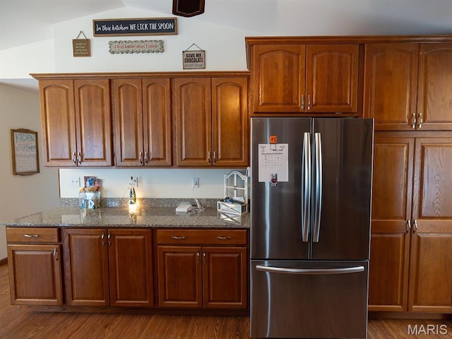 kitchen featuring freestanding refrigerator, dark stone countertops, dark wood-type flooring, brown cabinets, and vaulted ceiling