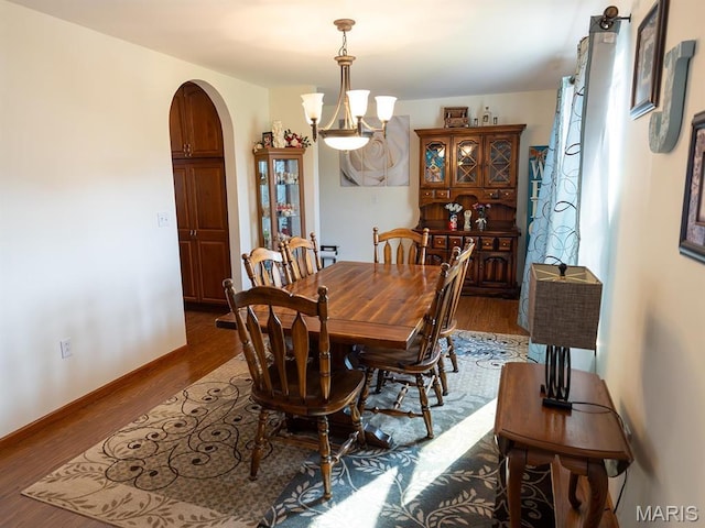dining area with a chandelier, arched walkways, dark wood-style flooring, and baseboards