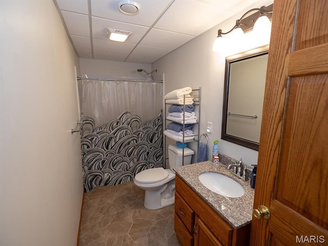bathroom with a drop ceiling, a shower with shower curtain, vanity, and toilet