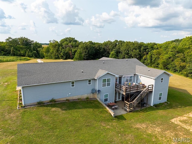 rear view of property featuring a deck, a patio, a lawn, and a view of trees