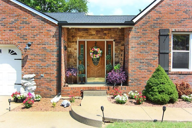 entrance to property with brick siding, a garage, and roof with shingles