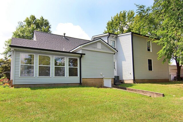 back of house featuring a lawn, cooling unit, and a shingled roof