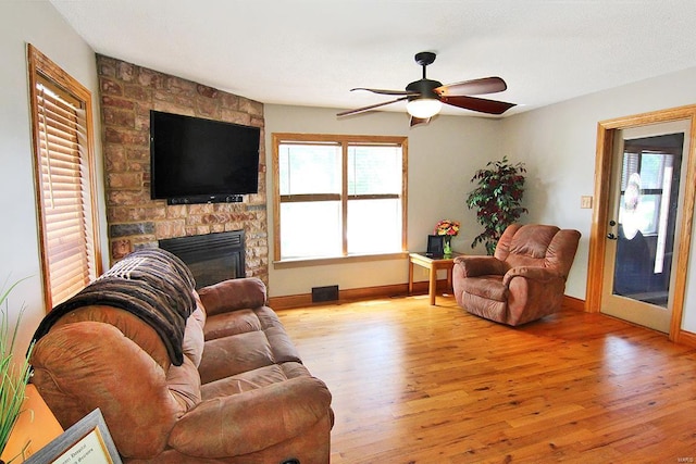 living area featuring wood finished floors, ceiling fan, a stone fireplace, and baseboards