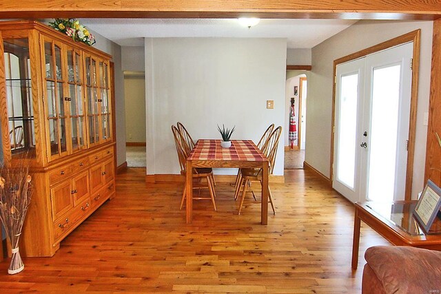 dining space featuring light wood finished floors, arched walkways, french doors, and baseboards