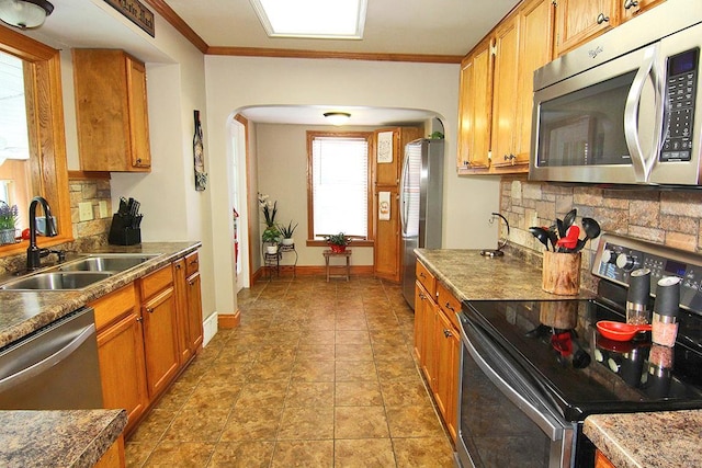 kitchen with stainless steel appliances, arched walkways, a sink, decorative backsplash, and brown cabinets