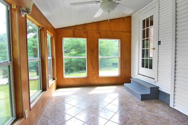 unfurnished sunroom featuring vaulted ceiling, wooden walls, and plenty of natural light