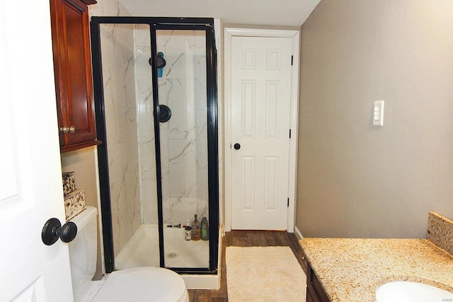 bathroom with a marble finish shower, toilet, wood finished floors, and vanity