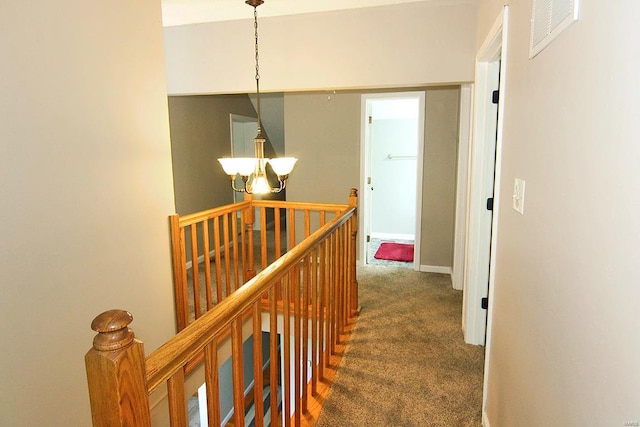 corridor with an upstairs landing, a chandelier, and dark colored carpet