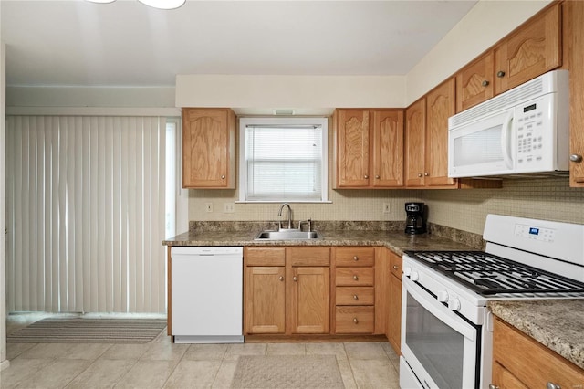 kitchen featuring white appliances, a sink, dark countertops, and brown cabinets