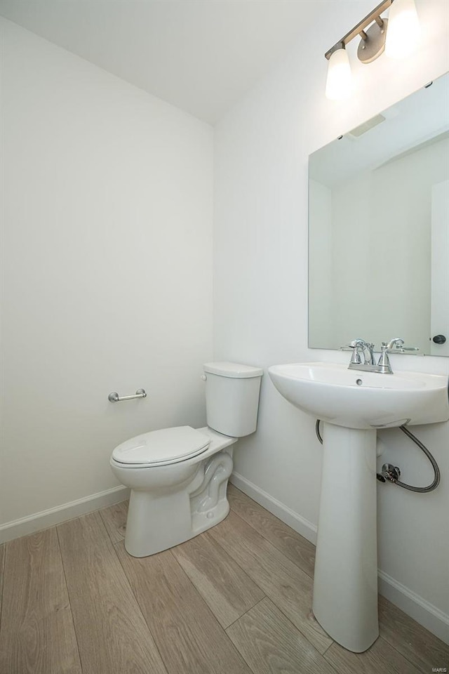 half bath with toilet, wood finished floors, and baseboards