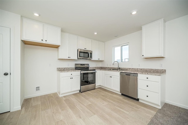 kitchen with stainless steel appliances, light stone counters, light wood-type flooring, white cabinets, and recessed lighting