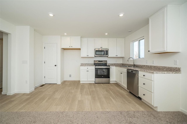 kitchen with appliances with stainless steel finishes, light wood-type flooring, a sink, white cabinetry, and recessed lighting