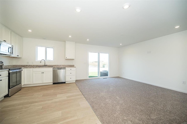 kitchen with stainless steel appliances, a sink, white cabinets, light wood-style floors, and recessed lighting