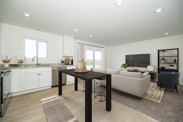 kitchen with dishwasher, a sink, light stone countertops, white cabinets, and recessed lighting