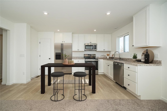 kitchen with appliances with stainless steel finishes, light wood-style floors, a breakfast bar area, white cabinetry, and recessed lighting