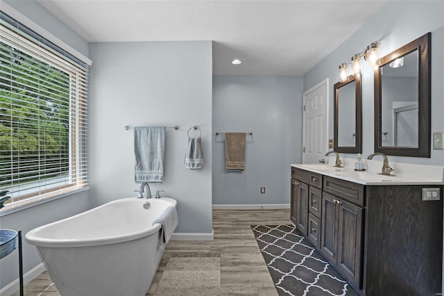 7102 Shadow Ln, Villa Ridge, MO 63089 - bathroom with baseboards, wood finished floors, a freestanding tub, double vanity, and recessed lighting