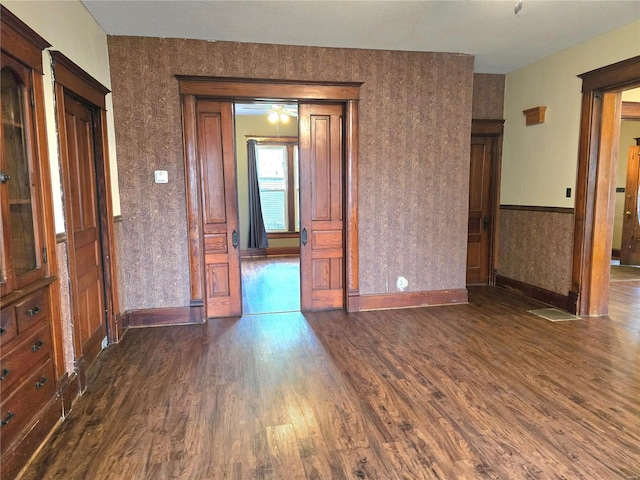 spare room featuring dark wood-type flooring, baseboards, wallpapered walls, and a ceiling fan