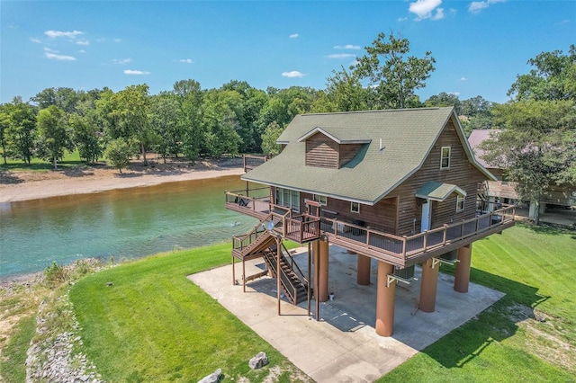rear view of house with a patio, a deck with water view, a yard, and a shingled roof