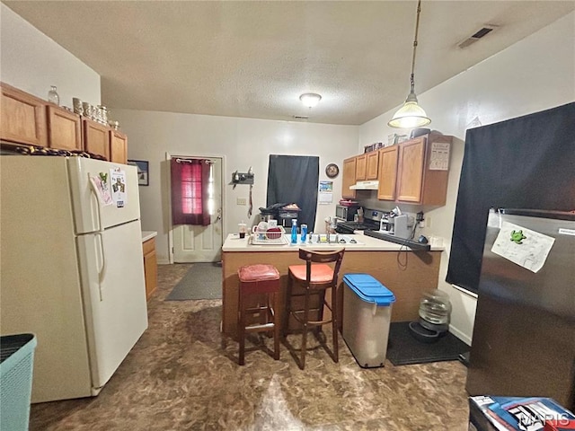 410 N Main St, Red Bud, IL 62278 - kitchen with freestanding refrigerator, a peninsula, a kitchen breakfast bar, brown cabinets, and under cabinet range hood