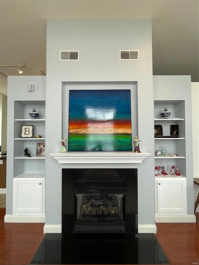 detailed view of built in features, a fireplace, rail lighting, baseboards, and wood finished floors