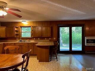 1742 Date Dr, Summersville, MO 65571 - kitchen featuring brown cabinetry, a peninsula, wood walls, a breakfast bar, and light countertops