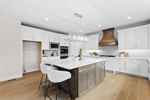 1315 Breezeridge Dr, Saint Louis, MO 63131 - kitchen featuring custom range hood, stainless steel microwave, double wall oven, a center island, and light wood-type flooring