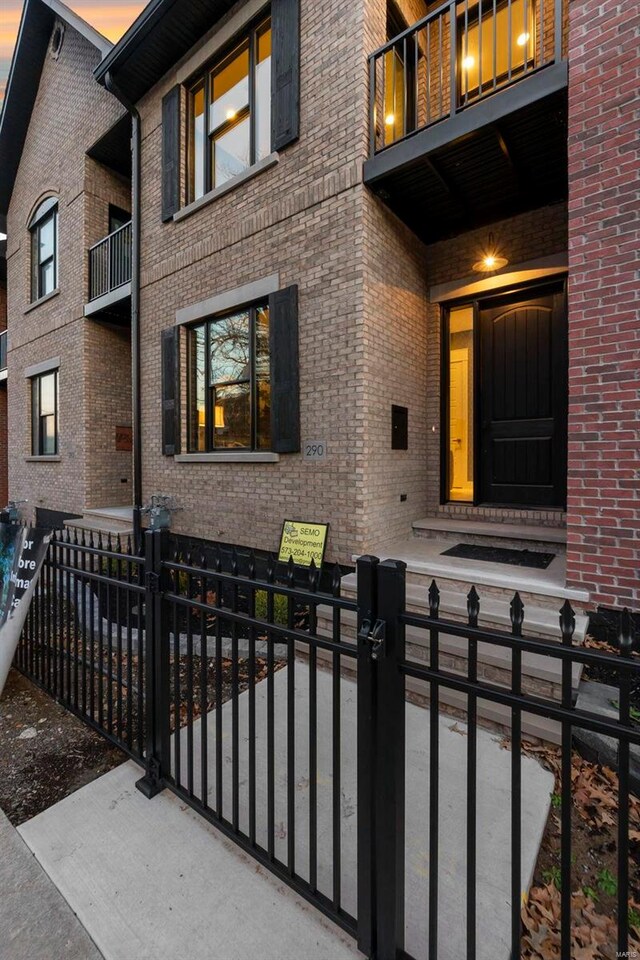 292 N Main St, Cape Girardeau, MO 63701 - exterior entry at dusk featuring a balcony, brick siding, a gate, and fence
