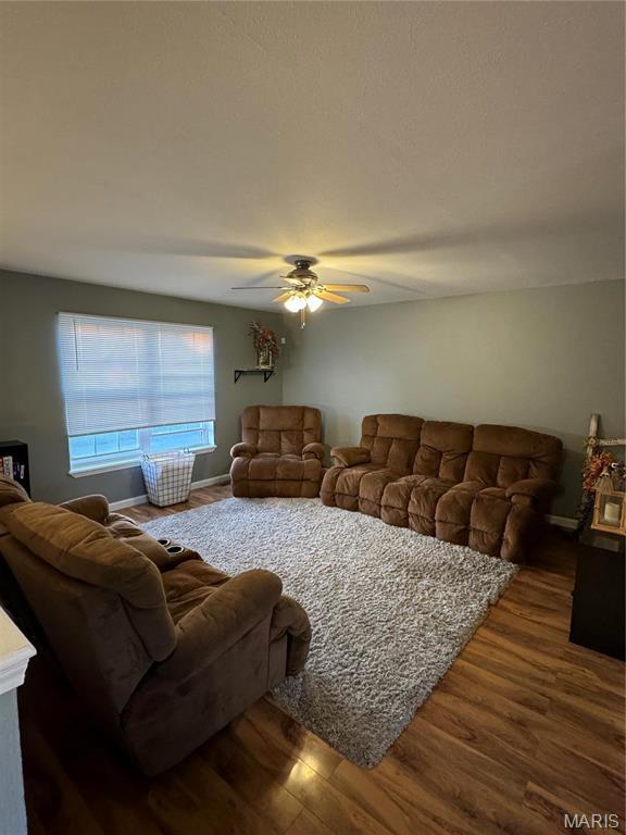 living area with dark wood-style flooring, ceiling fan, and baseboards