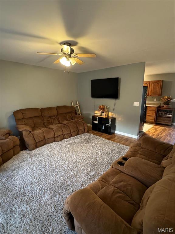 living area featuring light wood-style flooring, a ceiling fan, and baseboards