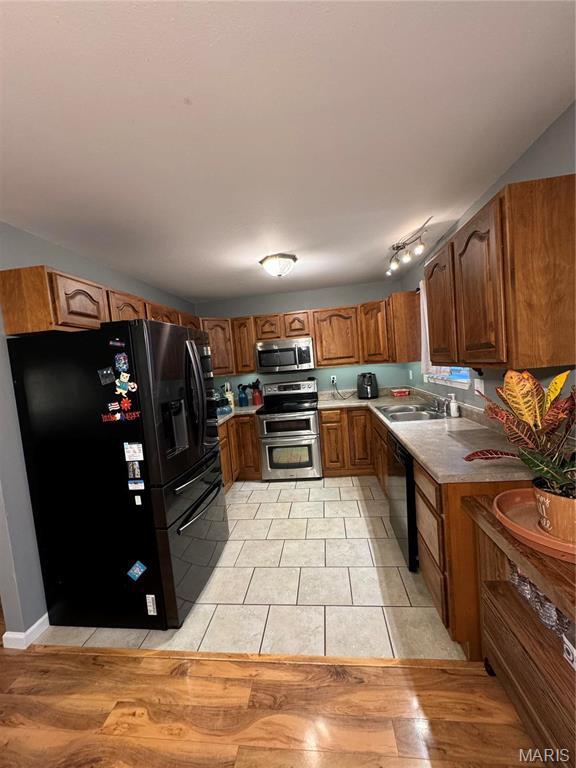 kitchen featuring black appliances, brown cabinetry, light countertops, light tile patterned floors, and a sink