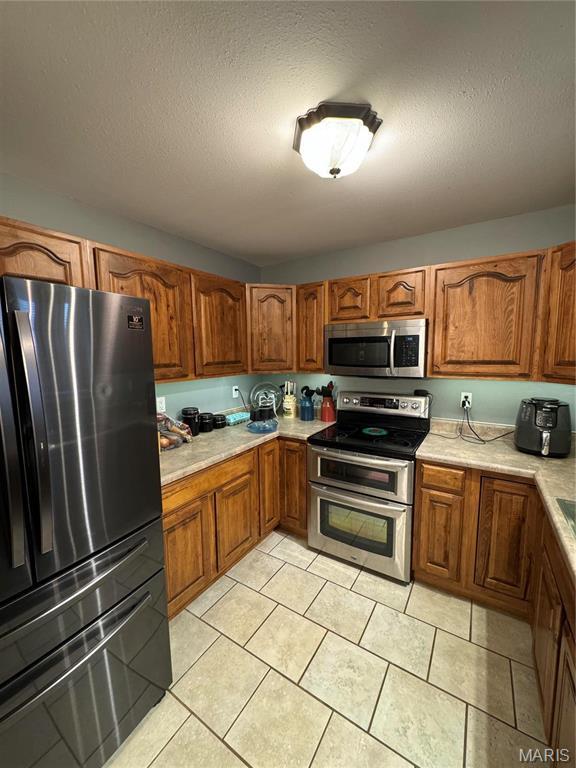 kitchen with appliances with stainless steel finishes, brown cabinets, light countertops, and a textured ceiling