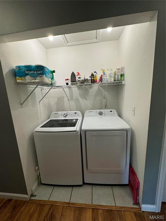 clothes washing area featuring washing machine and dryer, light wood finished floors, and baseboards