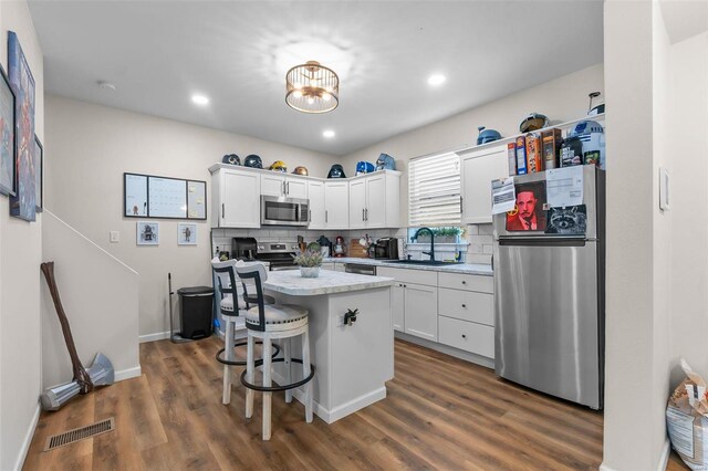 kitchen featuring stainless steel appliances, a sink, white cabinets, light countertops, and a breakfast bar