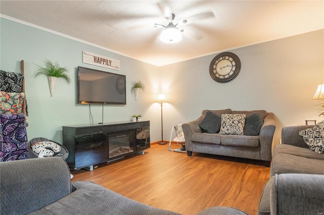 living area featuring crown molding, wood finished floors, ceiling fan, and baseboards