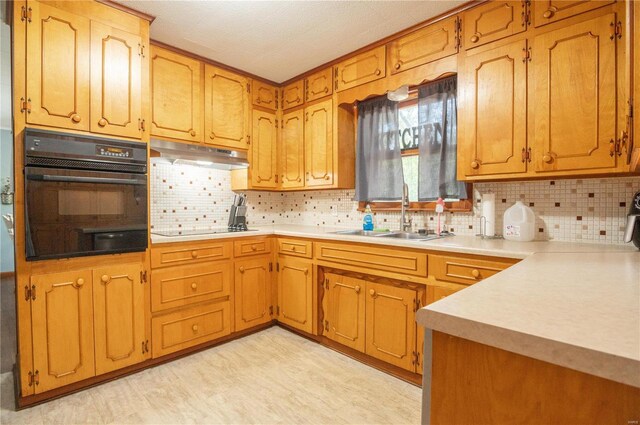 kitchen with black appliances, a sink, under cabinet range hood, tasteful backsplash, and light countertops