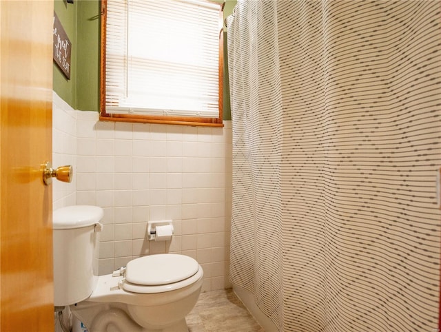 full bath with tile walls, toilet, curtained shower, and wainscoting