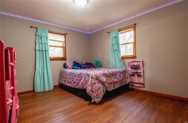 bedroom featuring multiple windows, wood finished floors, baseboards, and ornamental molding