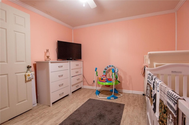 bedroom featuring crown molding, light wood finished floors, baseboards, a nursery area, and a ceiling fan