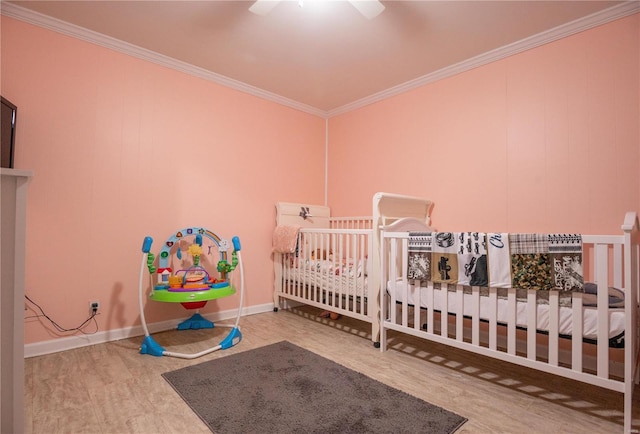 bedroom with wood finished floors, ornamental molding, a crib, and a ceiling fan