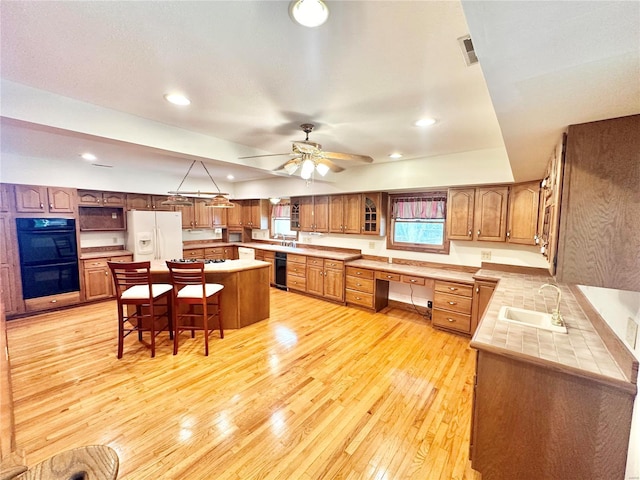 kitchen featuring black appliances, a sink, light wood finished floors, brown cabinetry, and recessed lighting