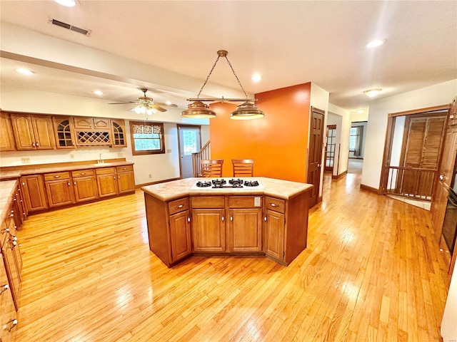 kitchen with light countertops, brown cabinets, light wood finished floors, white gas stovetop, and a kitchen island