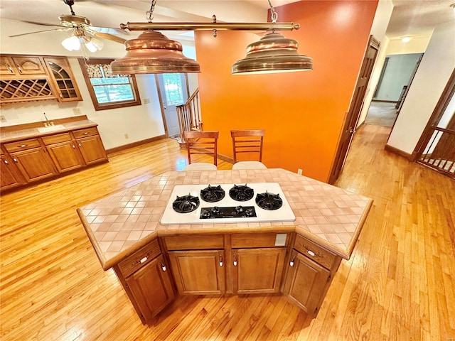kitchen featuring white cooktop, tile countertops, light wood finished floors, baseboards, and brown cabinetry
