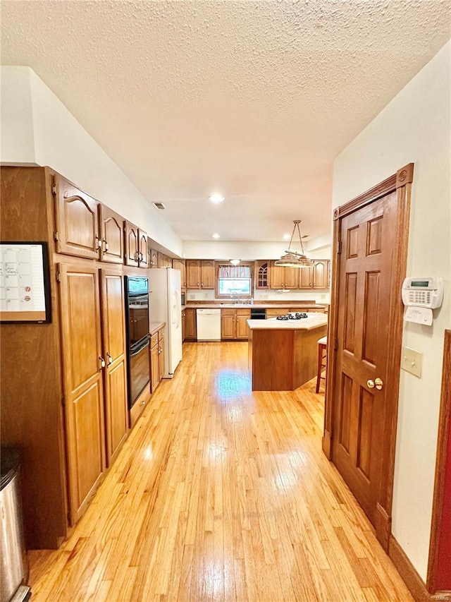 kitchen featuring white appliances, light wood-type flooring, a kitchen island, brown cabinets, and a textured ceiling