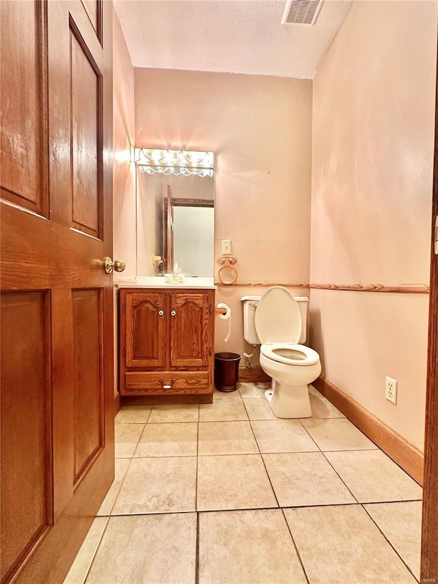 half bath with tile patterned floors, toilet, vanity, and baseboards