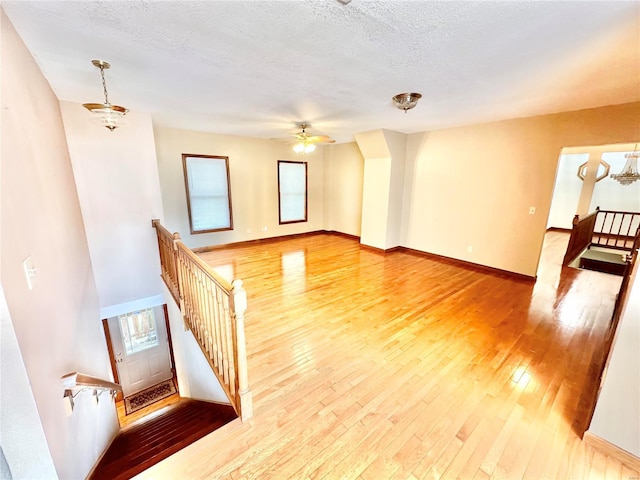 unfurnished living room featuring hardwood / wood-style flooring, a ceiling fan, a textured ceiling, stairs, and baseboards