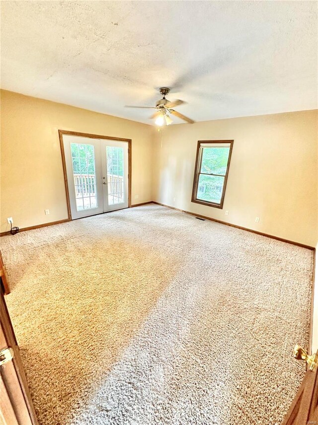 carpeted spare room with french doors, healthy amount of natural light, a ceiling fan, baseboards, and a textured ceiling