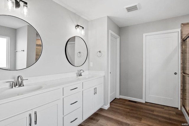 bathroom featuring wood finished floors, baseboards, double vanity, and an enclosed shower